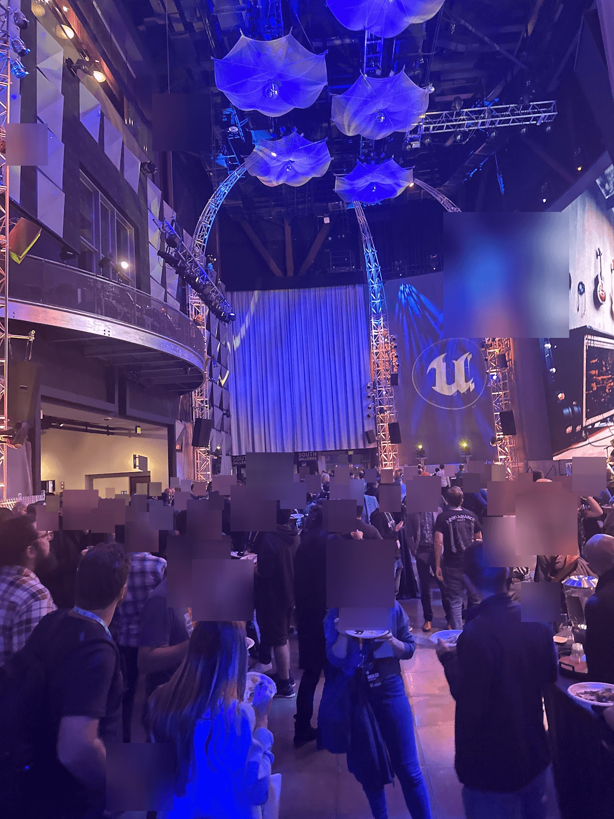 The Unreal Fest mixer at night with crowds gathered under blue umbrella lighting and the Unreal Engine logo on stage