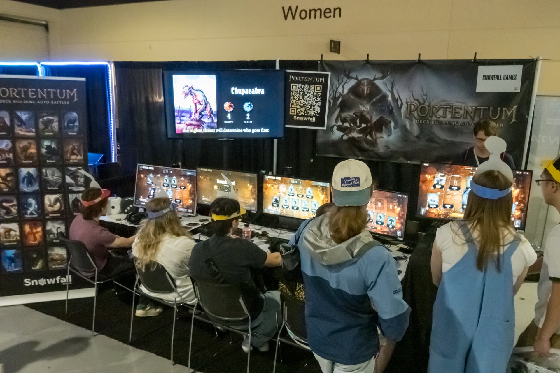 The row of booth PCs from the front, six monitors all running Portentum, under the Portentum banner and the Snowfall Games booth sign